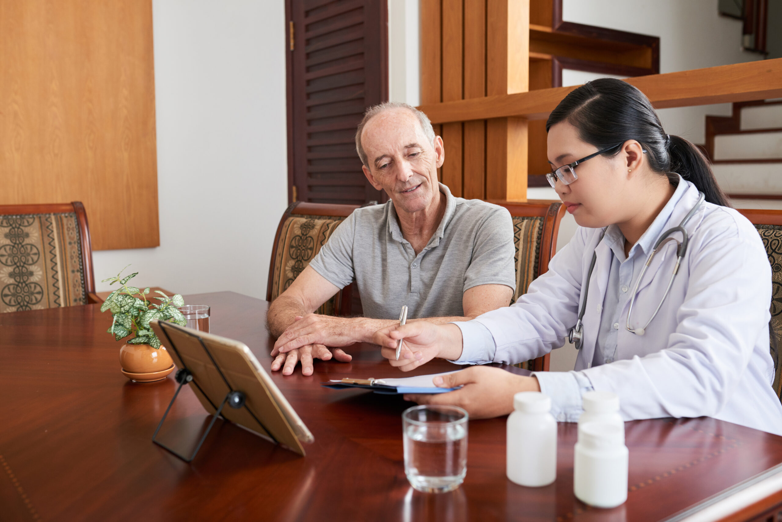 Adult woman sitting at desk with elderly man and talking about diagnosis reading clipboard