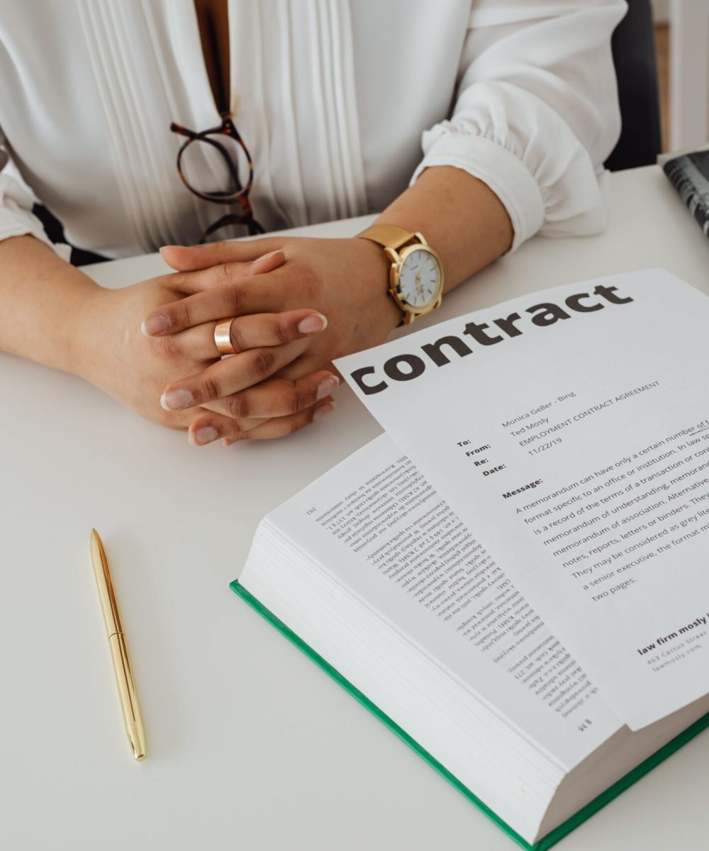 Businesswoman sitting at desk reviewing contract with legal documents and newspaper.