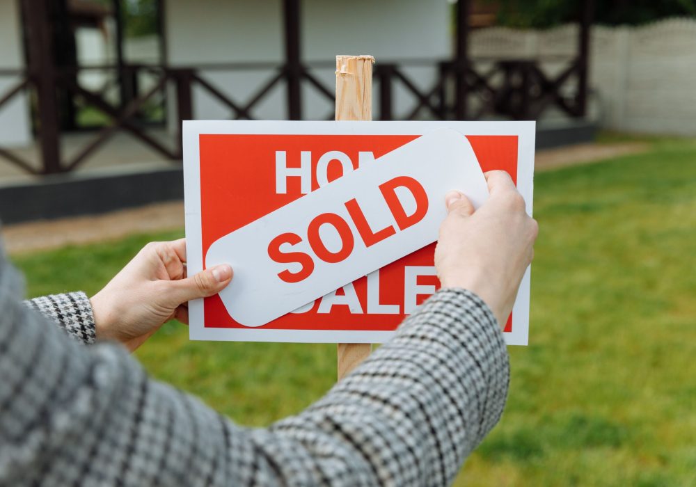 Close-up of hands placing a sold sticker on a real estate sign outside a house.