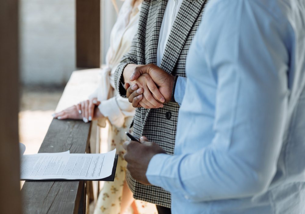 A close-up of hands shaking over a signed property agreement, symbolizing a successful real estate deal.
